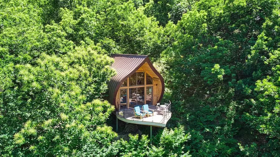 Vue aérienne de la cabane insolite La Châtaigne perchée dans les arbres en Ardèche, un hébergement atypique avec terrasse en bois au cœur d'une forêt verdoyante.