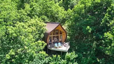 Vue aérienne de la cabane insolite La Châtaigne perchée dans les arbres en Ardèche, un hébergement atypique avec terrasse en bois au cœur d'une forêt verdoyante.