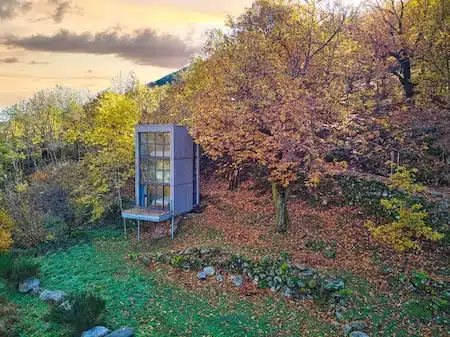 Cabane insolite contemporaine en Ardèche avec grande verrière, vue aérienne d'un hébergement atypique niché en lisière de forêt aux couleurs de l'automne