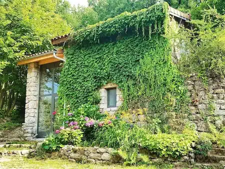 Façade de l'hébergement insolite en pierre La Louve aux Cabanes du Loup Bleu, habillée de végétation et de fleurs